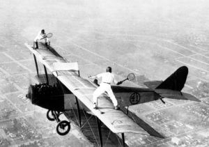 Black and white photo of two men playing badminton atop the wing of a biplane in 1925. 